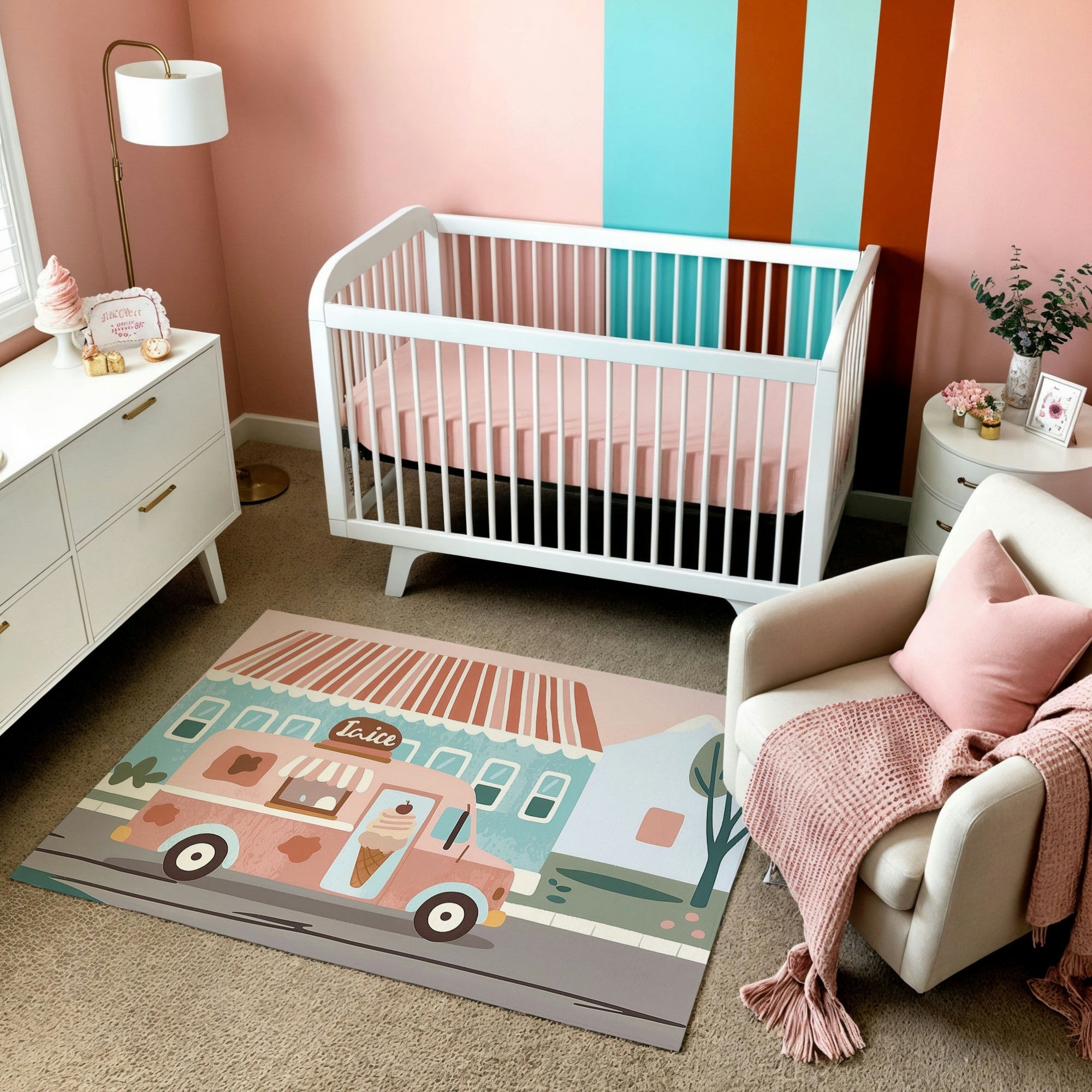 A pastel-themed nursery with a white crib, pink bedding, and a cozy armchair draped with a pink throw blanket. The floor features a playful rug depicting a retro pink ice cream truck in front of pastel-colored houses, adding a whimsical touch to the room. The walls are painted in soft pink and teal stripes, complementing the light and airy decor.