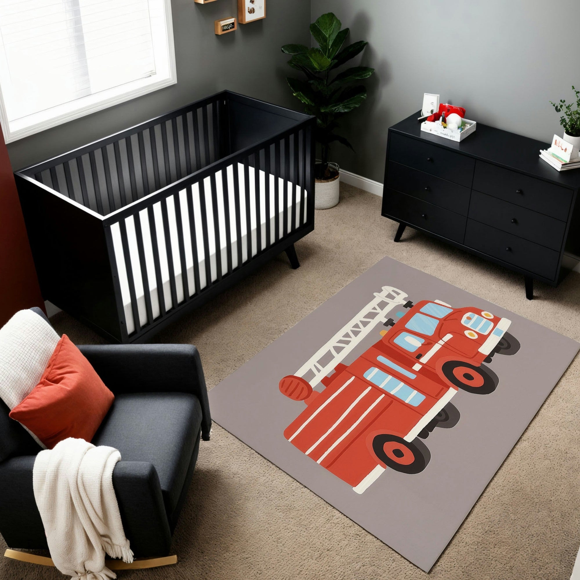 A modern nursery featuring a black crib and dresser against a gray wall, complemented by a charcoal armchair with a red pillow and white knit throw. The room includes a playful area rug with a bright red fire truck illustration, complete with a ladder and vibrant details. A leafy green plant and minimal decor add a cozy touch to the sleek, firehouse-inspired design.