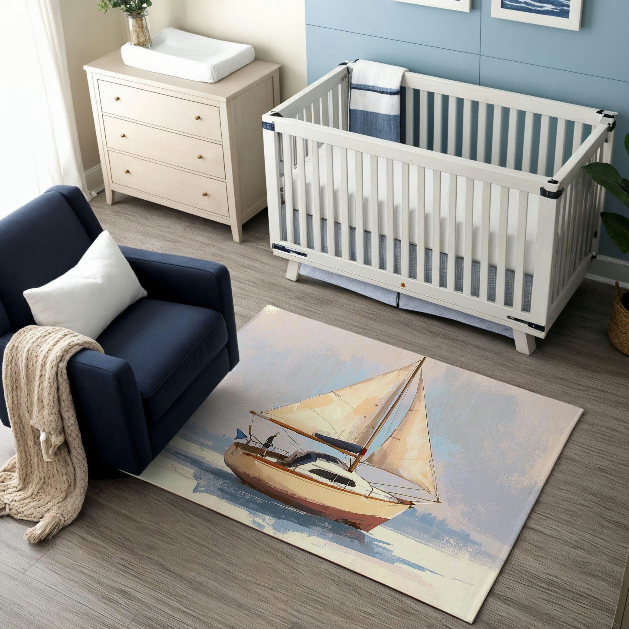 A nautical-themed nursery featuring a white crib with blue bedding against a light blue accent wall, complemented by a beige dresser with a changing pad on top. The room includes a navy-blue armchair with a white pillow and a cozy knit blanket draped over the side. A statement area rug showcases a beautiful sailboat illustration, adding a serene and coastal vibe to the space.